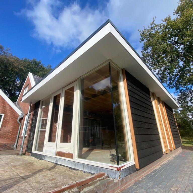 Moderne aanbouw van een huis met grote ramen en een overhangend dak.